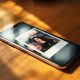 An iPhone 17 resting on a warm wooden desk surface, screen displaying a grainy vintage-style Polaroid selfie with a white border and soft light leak, shot at a 45-degree angle using a 50mm lens, soft natural window light from the left casting long diffused shadows, realistic glass reflections on the screen, shallow depth of field, no hands, no people, no watermark, photorealistic, 16:9