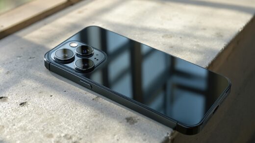 iPhone 18 Pro resting on a warm grey concrete surface, rear triple-lens camera system visible,