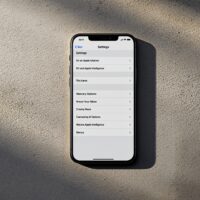 iPhone 17 Pro lying flat on a warm grey concrete surface, Settings app open showing a Siri and Apple Intelligence menu with multiple AI options listed, soft cinematic side lighting with long directional shadows, no hands, no people, no text visible on screen labels, photorealistic, 16:9